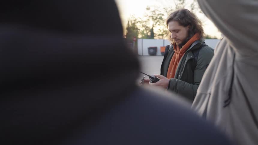 A woman hands a small group of people walkie talkies in a parking lot outside