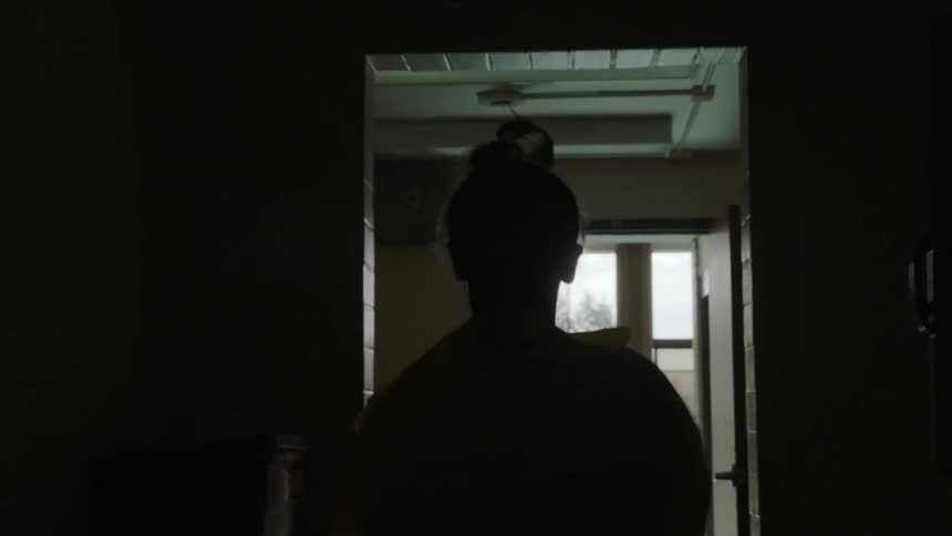 Woman walks down a dark hallway out the door
