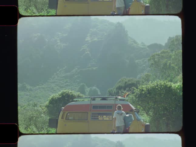 Framed by film strip edges a surfer carries his board and a bag walking along a roadside towards a vintage van parked near a lush mountainous area