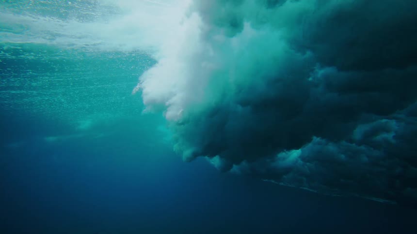An underwater view of the foamy turbulent underside of a wave as it crashes into the deeper darker blue water below