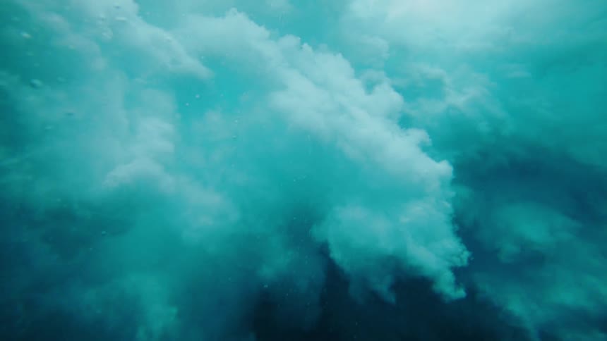 An underwater perspective captures the dynamic movement of a wave as it breaks showing the textured surface of the water and the churning foamy turquoise depths