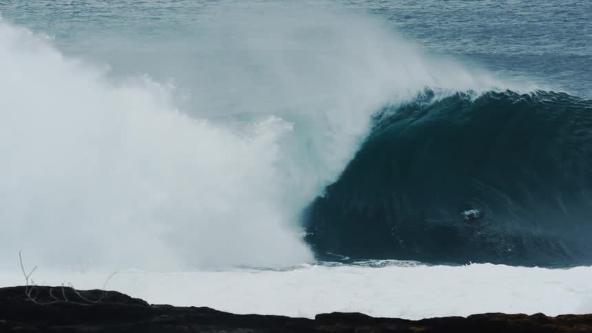Surfer performing on a big tubular wave and three other people filming and watching
