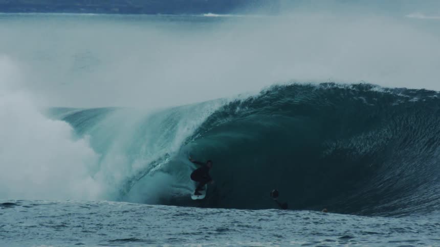 A man is surfing in a huge wave
