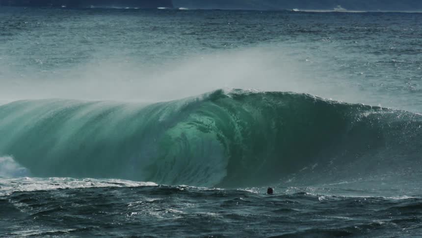 A man is on a surfboard watching as a large wave breaks in front of him