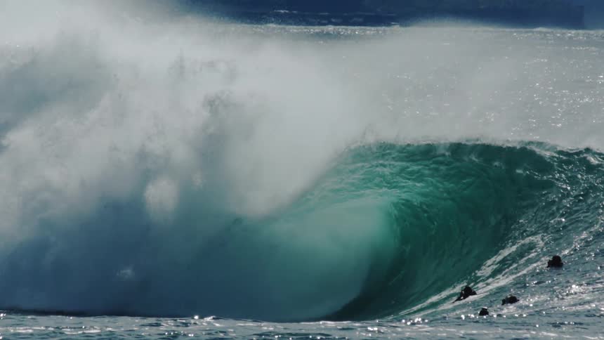 Surfers are on their boards waiting as a large wave crashes over them