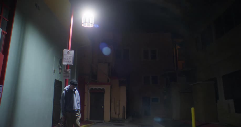 Man leaning against a lamppost in the middle of an alley at night