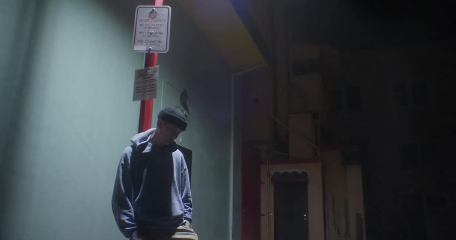 A man is leaning against a street light in front of a building