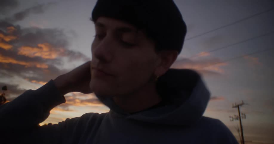 A young man rubs his face while standing outdoors at sunset