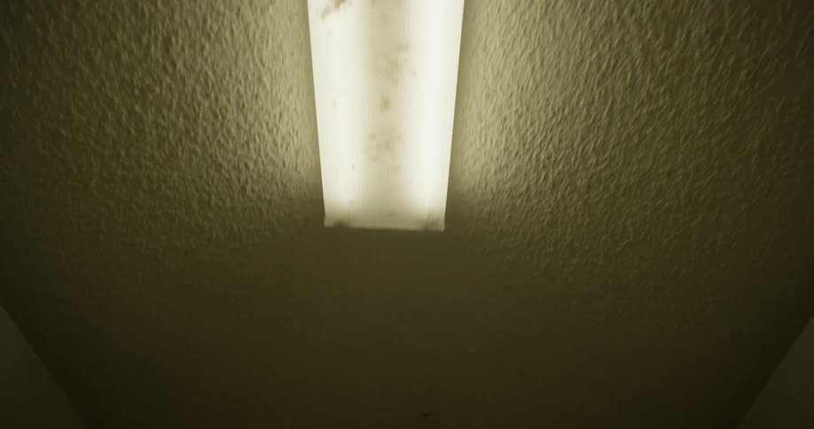 A fluorescent light fixture is briefly visible against a dim textured ceiling