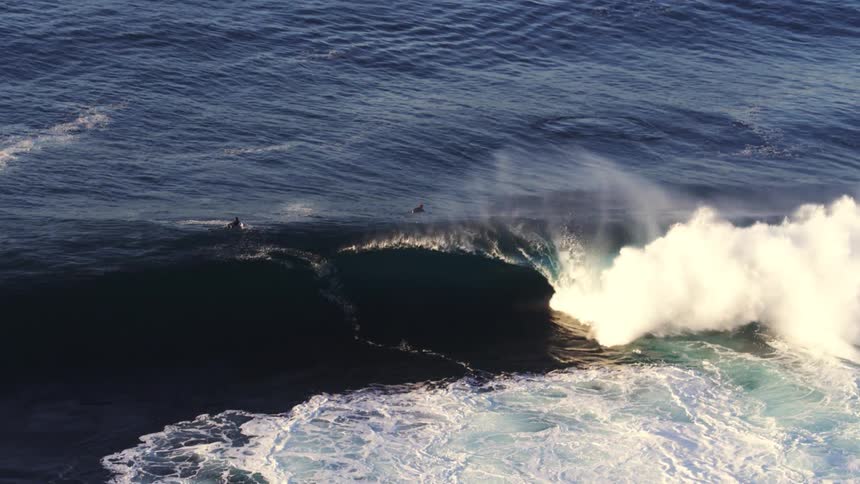 Surfers paddleboarding into a crashing wave