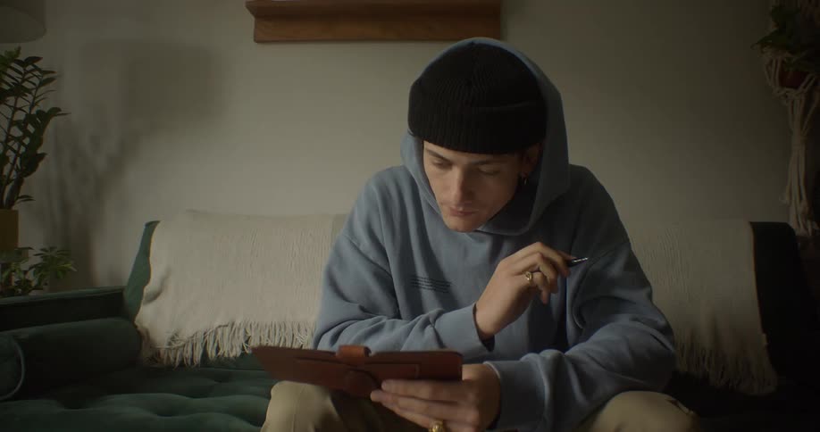 A young man sits on his sofa and writes in a checkbook