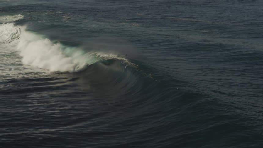 A surfer wearing a wetsuit is paddling on a surfboard to catch and ride an approaching wave