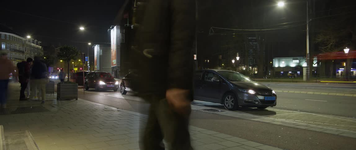 Busy city street and sidewalk at night with time lapsed movement of cars and people coming and going