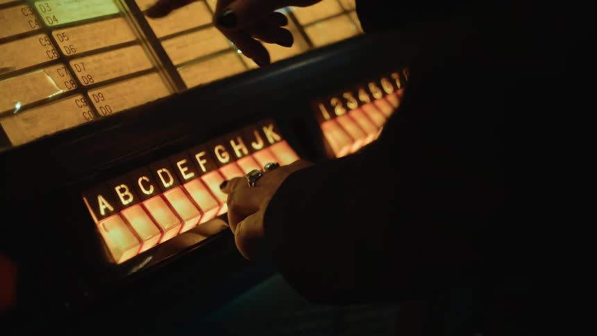 A woman wearing rings points to the menu on an old jukebox and makes a selection