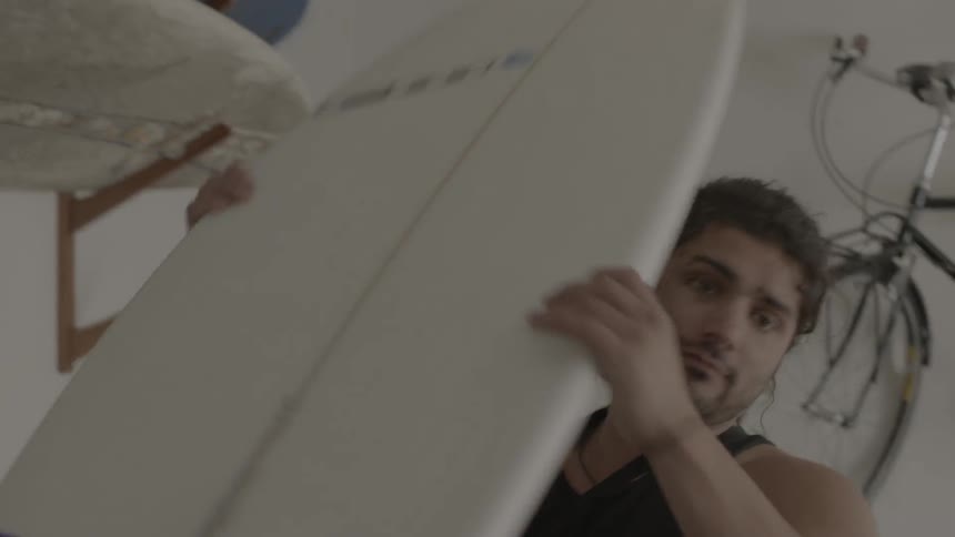 A man removes a surfboard from a wall rack