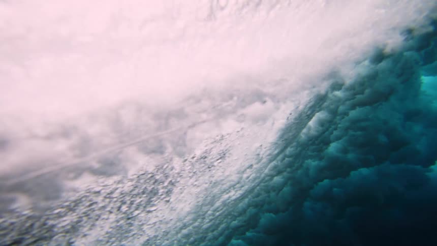 From beneath the ocean surface a powerful wave breaks and crashes overhead above a coral reef