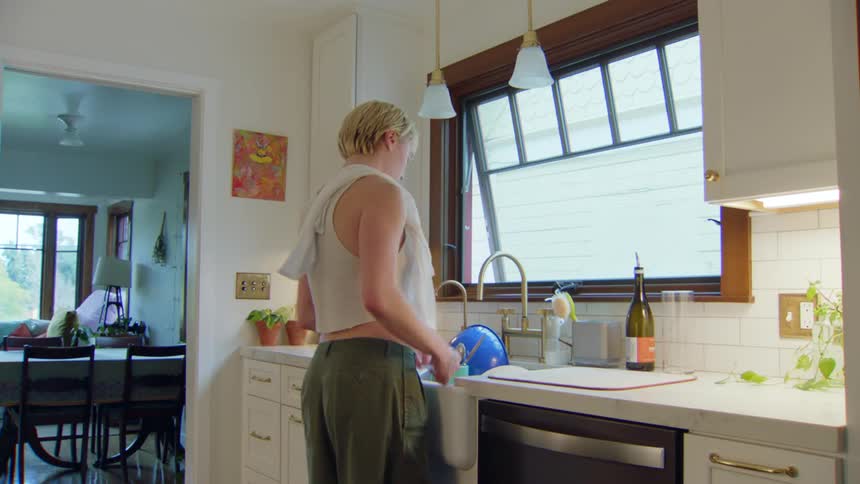 A young woman washes dishes while standing at the kitchen sink