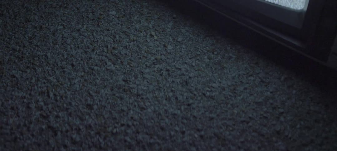 A tv screen playing white noise reflects on the asphalt ground beneath it