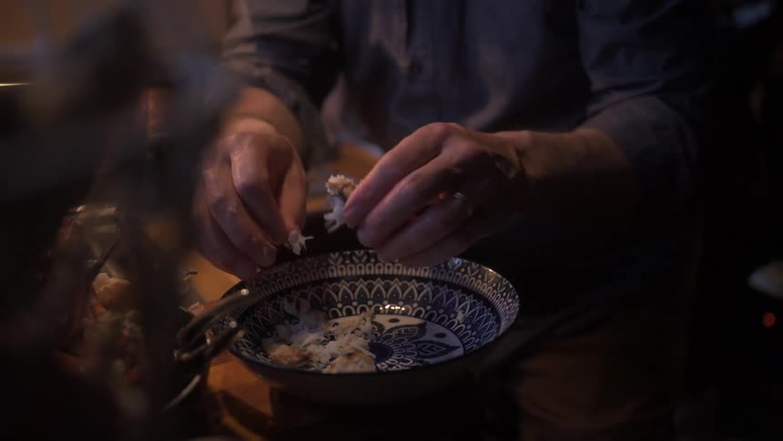People tear crab meat apart over a decorative bowl filled with similar food pieces in a simple kitchen setting