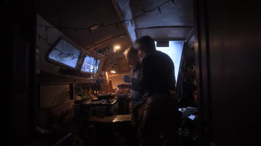 Two men are in the kitchen of a boat preparing food