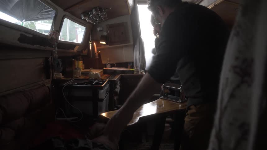 A man and woman move things around in the kitchen of a boat