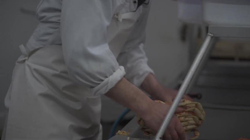 A cook wearing an apron is in a kitchen at the sink cleaning a crab