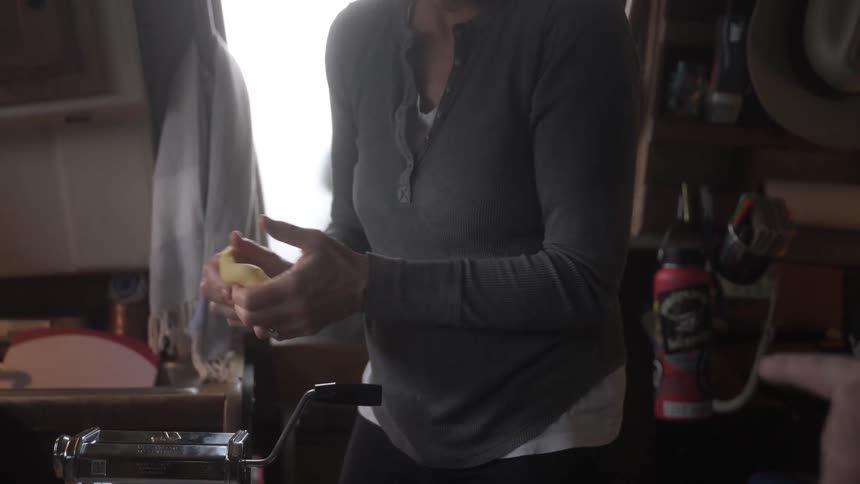Person points toward the counter while a woman works with dough in the kitchen during the day