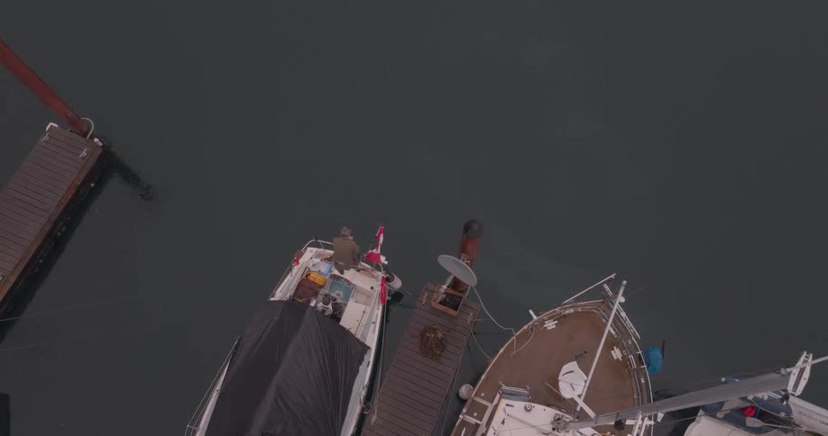 An aerial view captures two boats docked at a pier with one person visible on the deck of the left boat bearing a canadian flag