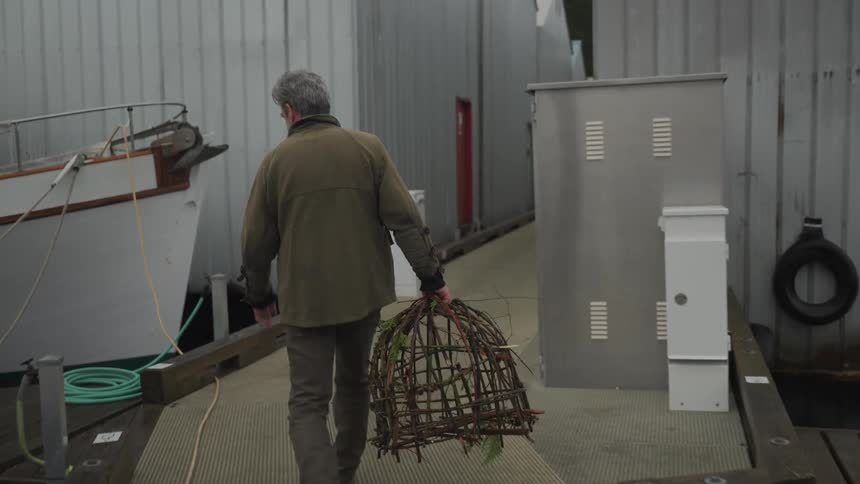 View of a man from behind walking with a fishing trap