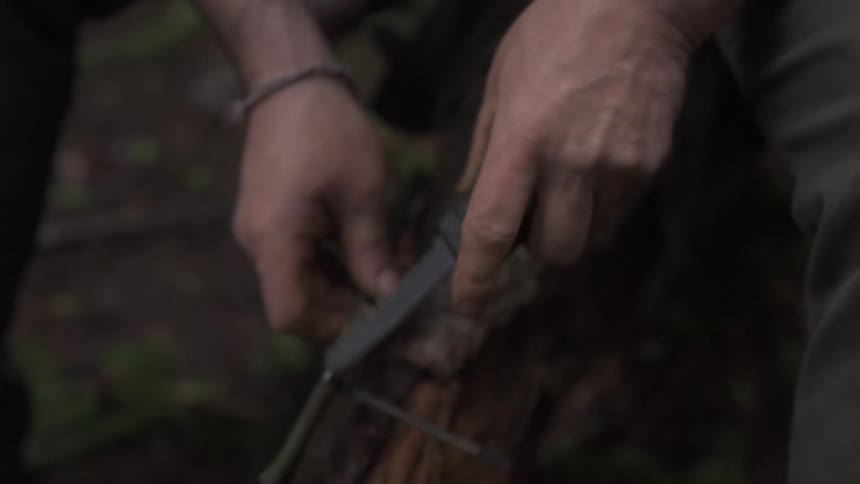 Pair of hands handling a knife on a piece of wood