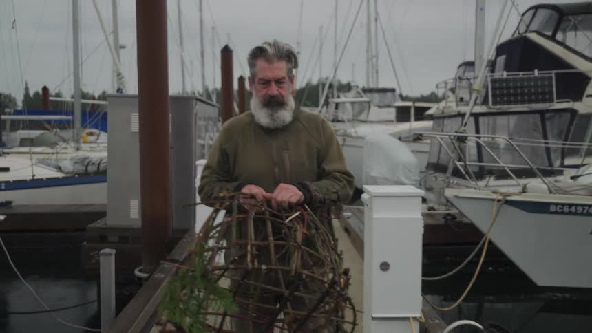Man walking on a pier at a marina carrying a fishing trap