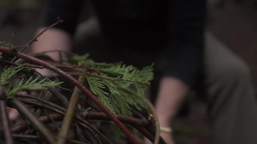 A closeup of a person weaving a round handcrafted basket from fresh twigs in a serene natural setting