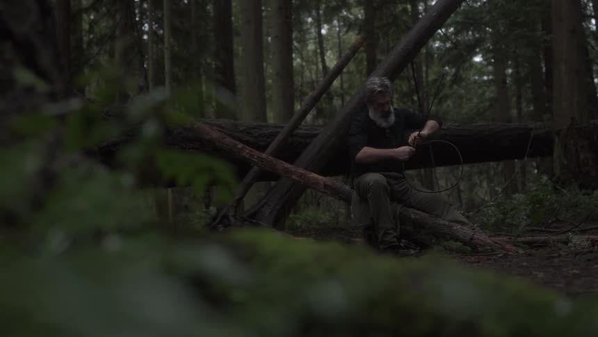Man sitting on a log in the forest with a wooden bow