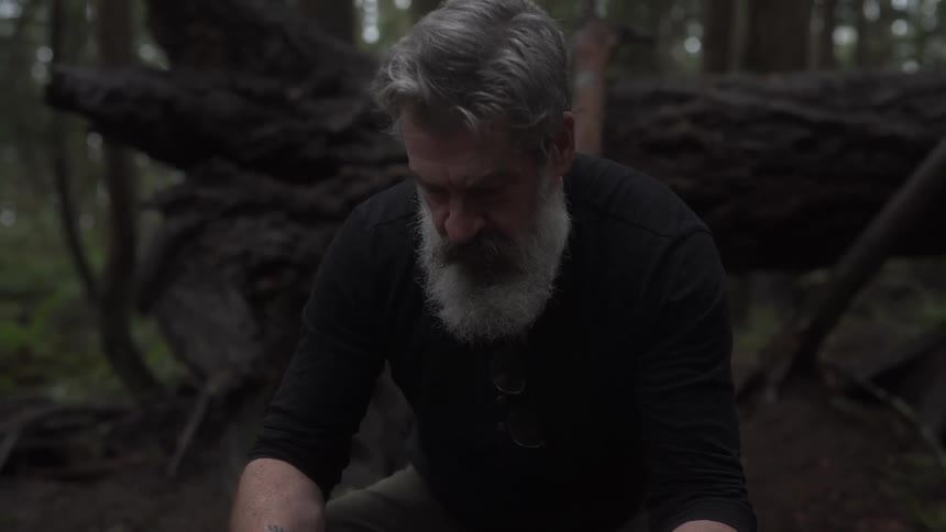 A man is crouching by a fallen tree