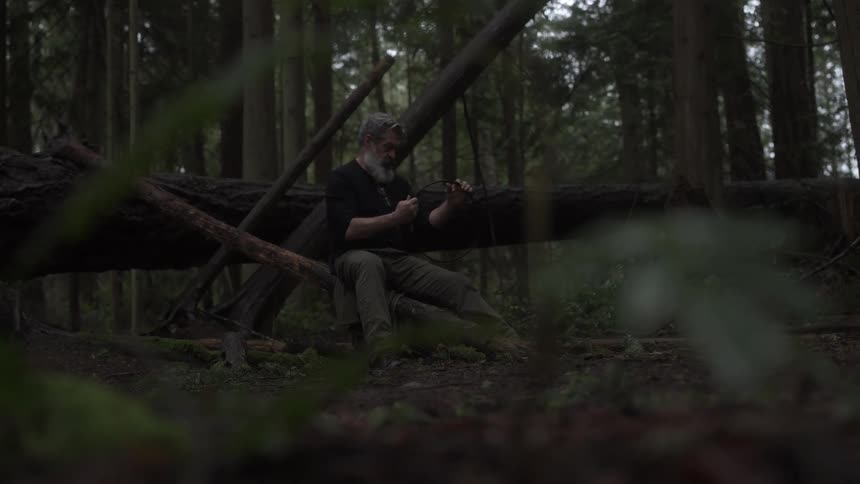 Man sitting in the forest making a bow