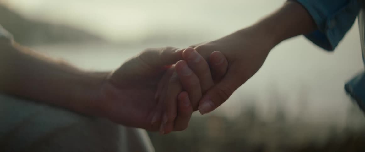 A closeup captures two hands gently holding one thumb softly rubbing the back of the other hand with the background blurred