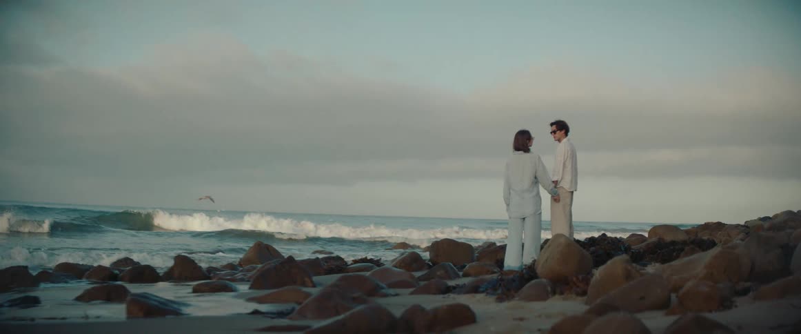 Couple holding hands as they stand on rocks at the edge of a beach