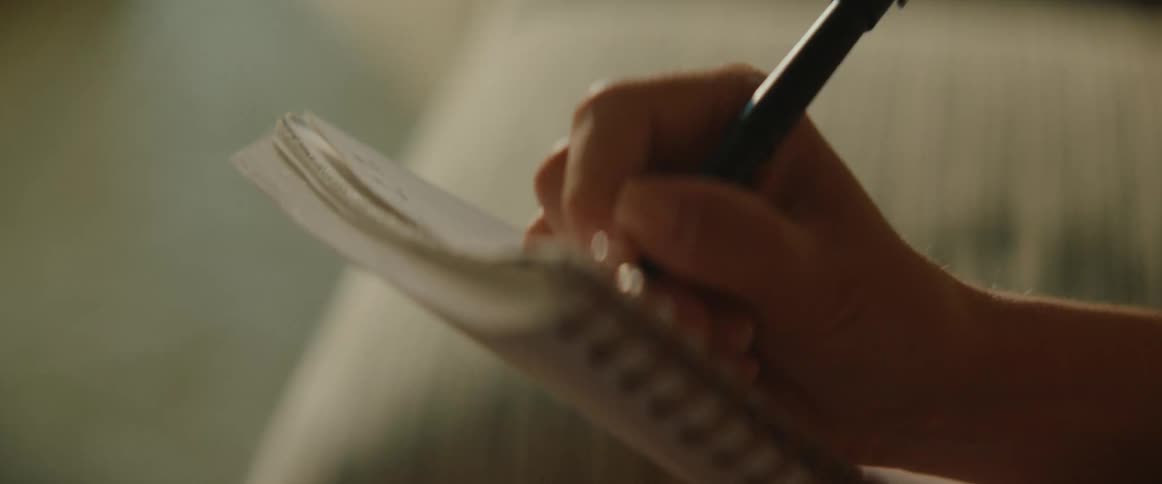 Woman with glasses focused writing in a notebook