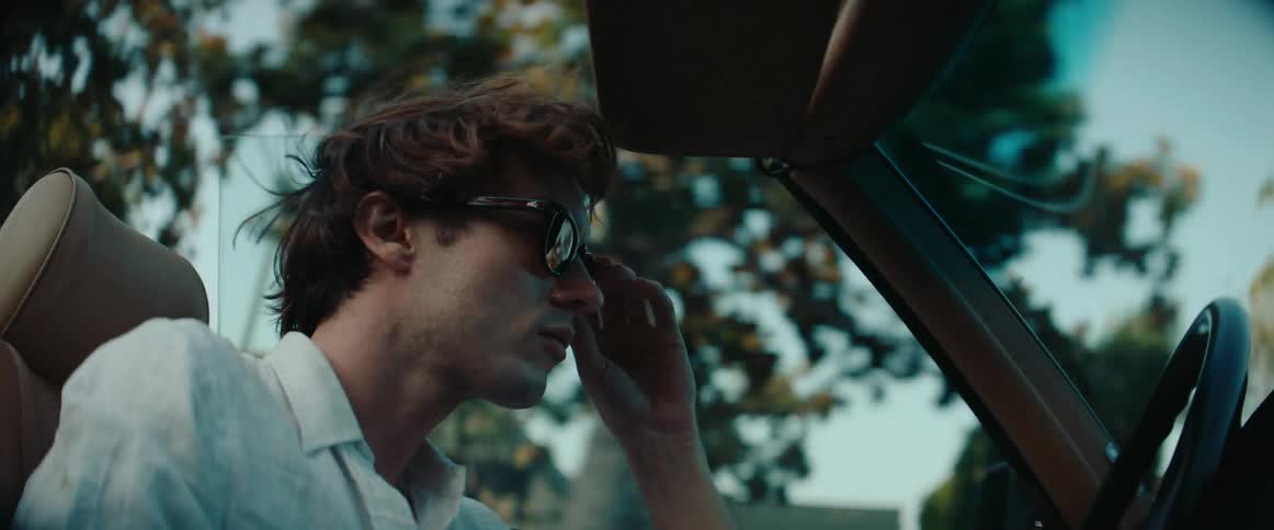 Man putting on sunglasses while driving a convertible vehicle