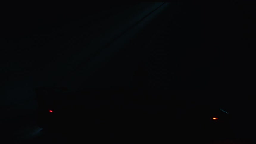 A person stands next to a sleek dark sports car with illuminated orange lights is silhouetted against a deep blue backdrop