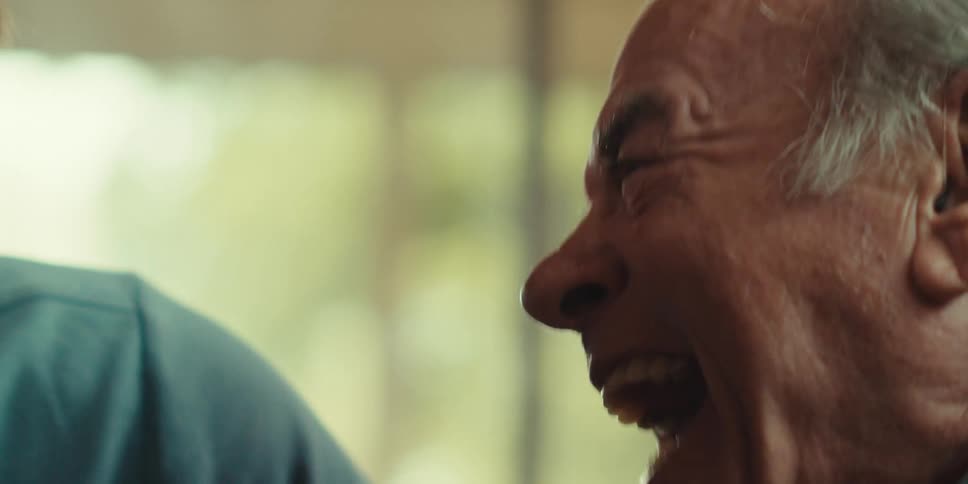 A closeup of an elderly man laughing and celebrating joyfully with someone beside him at home