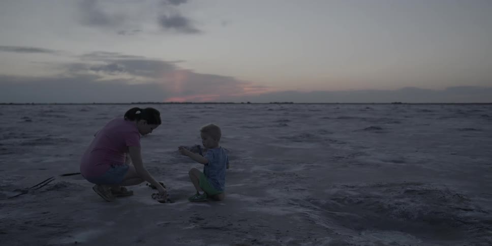 Woman and child dig in the sand at sunset