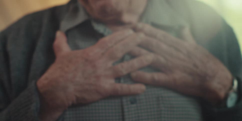Elderly man gestures with his hands and smiles while talking indoors during the daytime