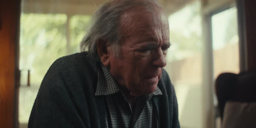 Elderly man stands frowning in his living room on a sunny day
