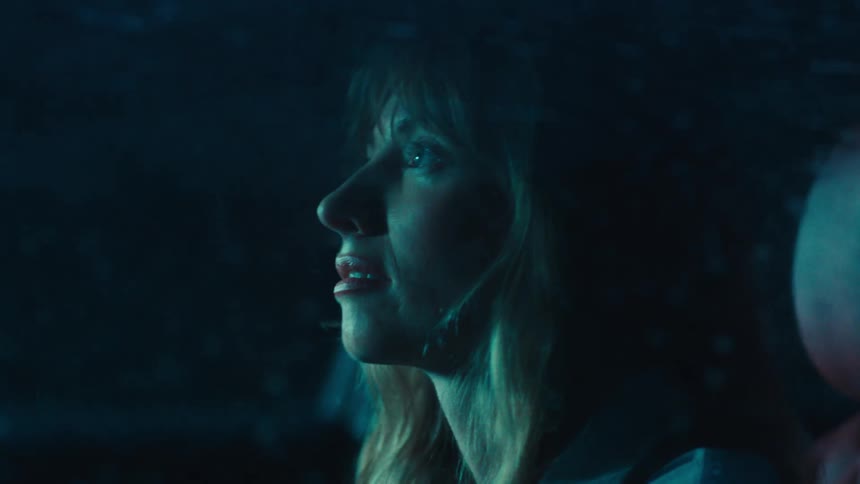 A closeup of a woman sitting in the drivers seat gazing through the windshield as heavy rain pours outside at night