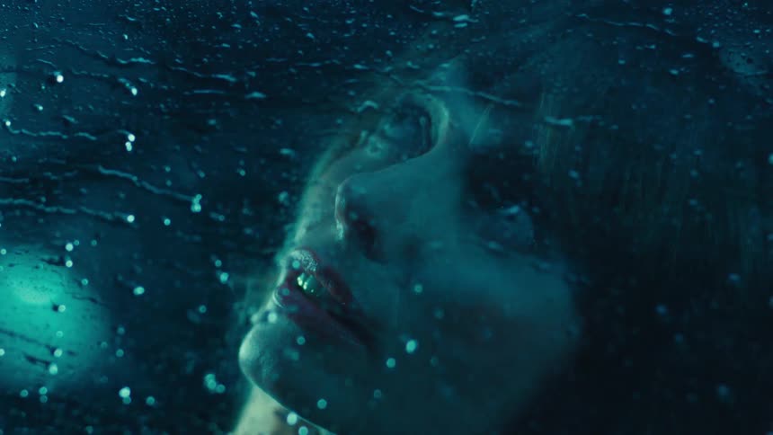 Woman looks out the window while raindrops flow across the glass during a storm