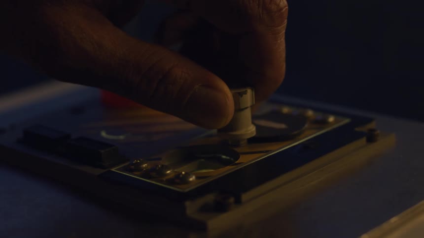 A hand adjusts a small metallic knob on a board surrounded by various electronic parts and connections