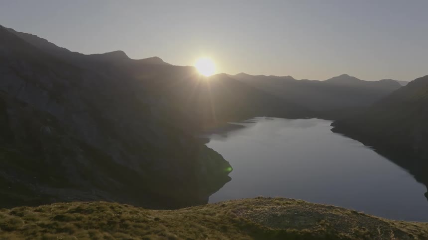 Sunrise on the horizon over a lake surrounded by mountain range
