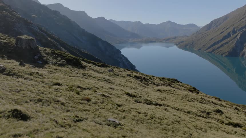 Crystal clear lake reflecting surrounding mountains in a tranquil landscape with clear skies and a hillside covered in undergrowth