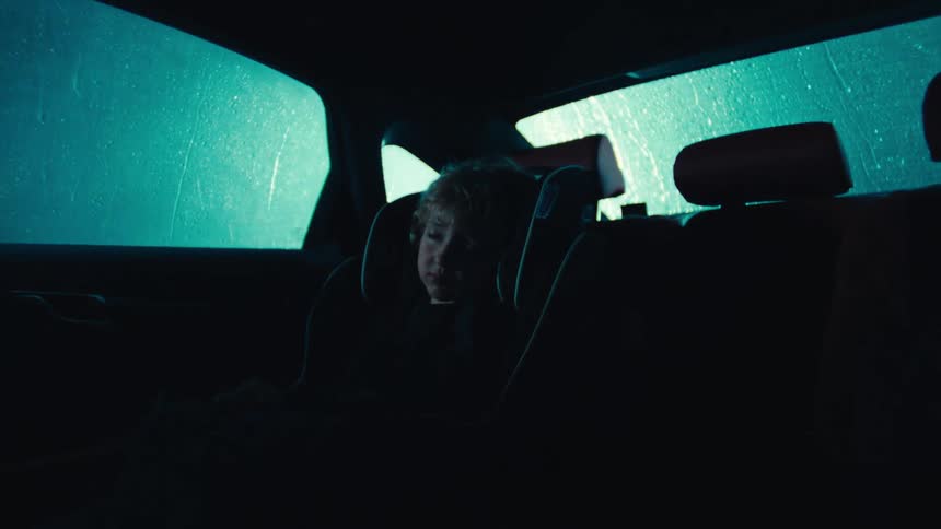 A little boy is sleeping in his car seat as the car moves